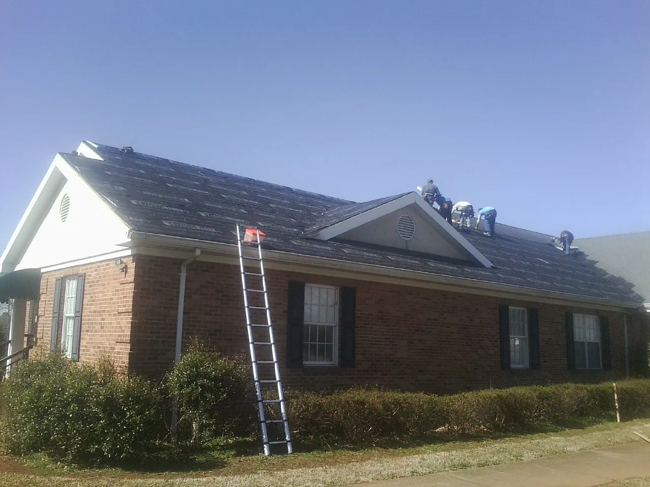 Crew tearing shingles off a brick ranch roof with a ladder set — Emergency Roof Repair work by our crew in Glenford