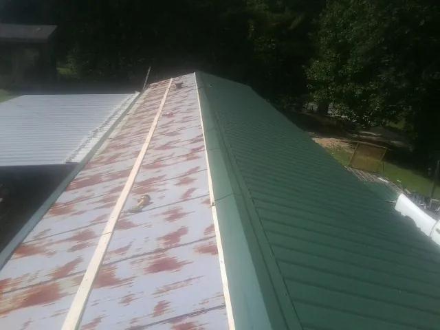 Old rusted panels beside newly installed green metal roofing — Wind Damage Roof Repair by Roofing Brothers in Glenford