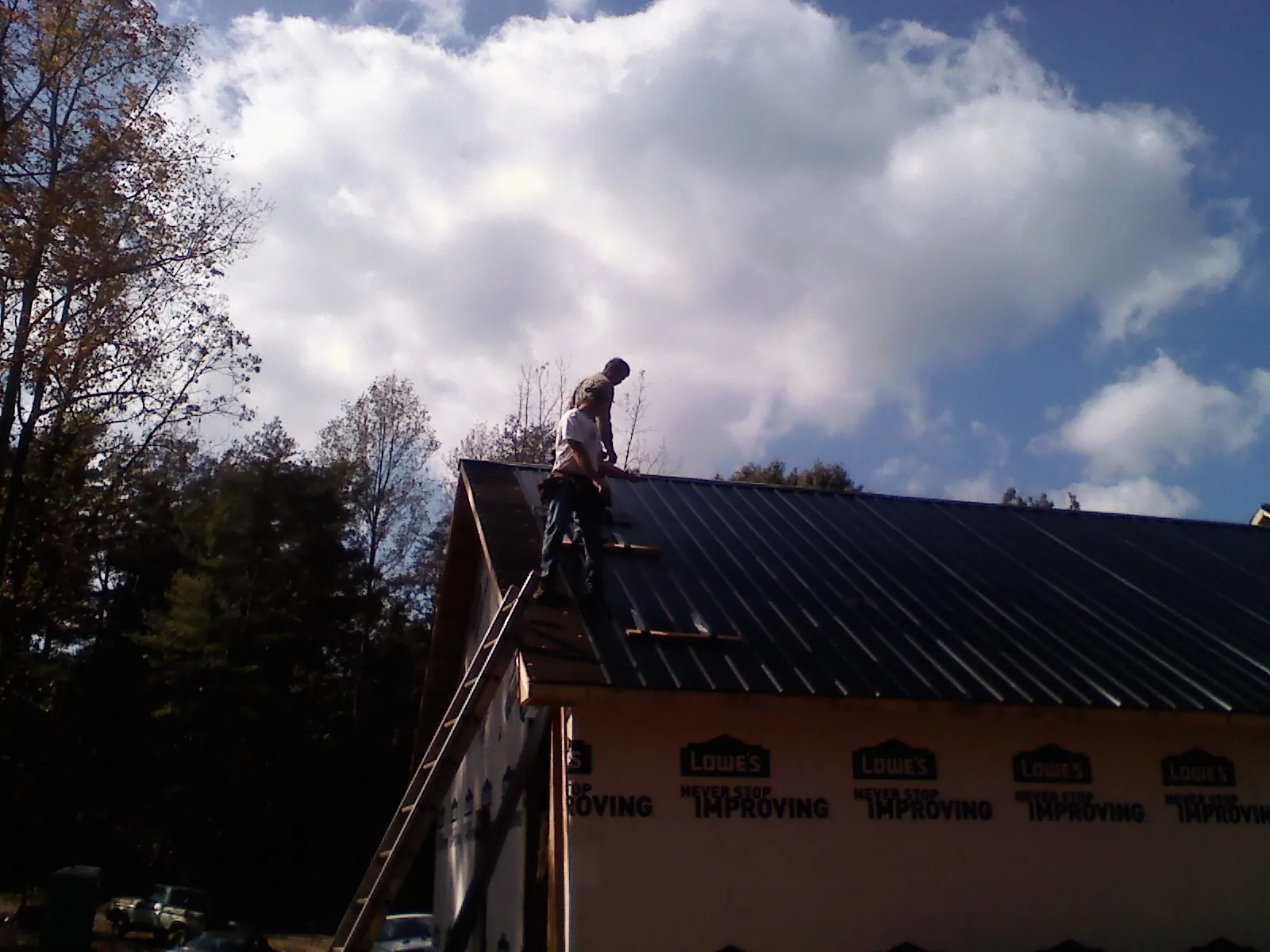 Roofer fastening dark metal panels high against a cloudy sky, from a Roof Inspection job in Glenford
